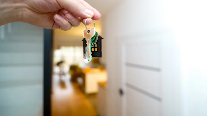 A hand holding house keys in front of a door